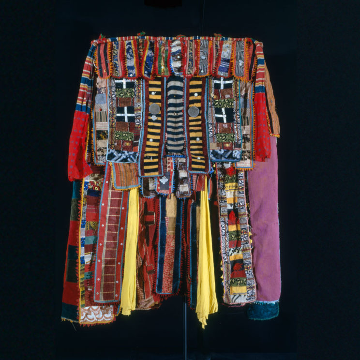A large cloak to cover the entire body is comprised of strips of fabric, each adorned with patterned cloth, mirrors and medallions.